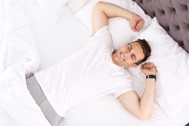 Young man after sleeping in bed at home, top view