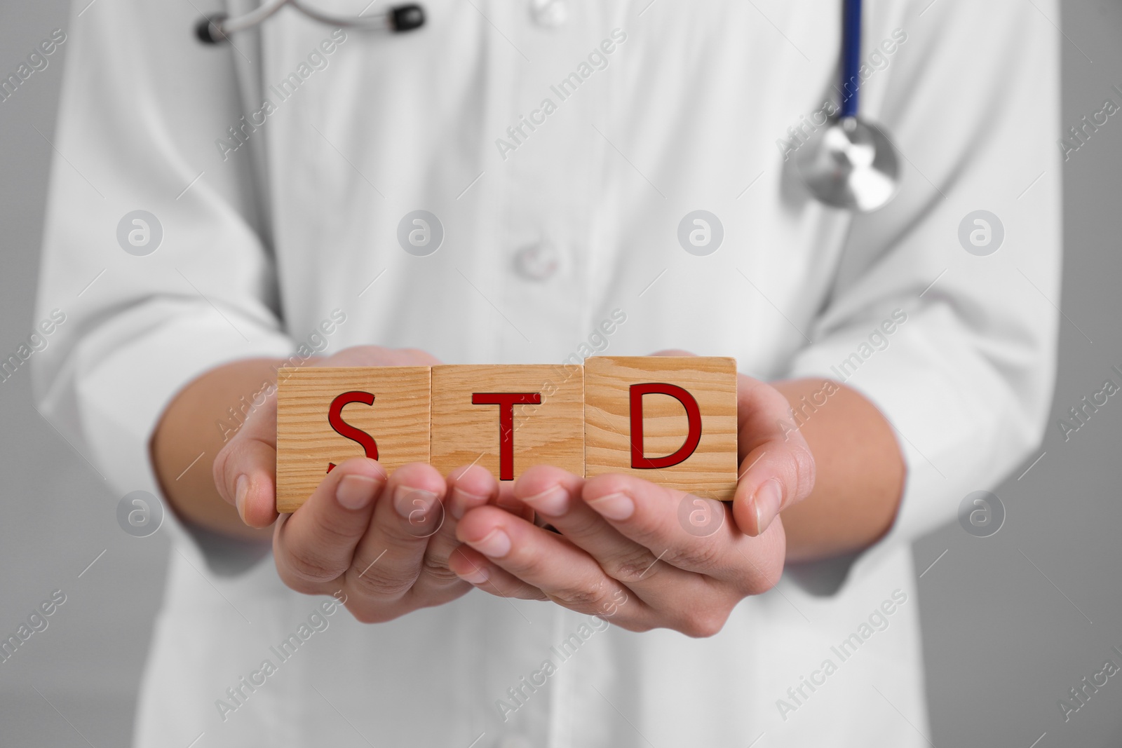 Photo of Doctor holding wooden cubes with abbreviation STD on grey background, closeup