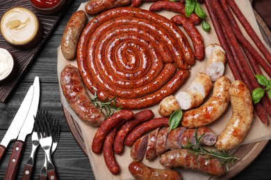 Photo of Different delicious sausages with herbs and sauces on black wooden table, flat lay. Assortment of beer snacks