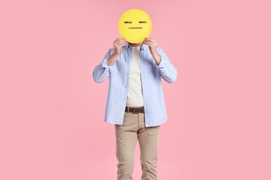 Photo of Man holding emoticon with closed eyes and mouth on pink background