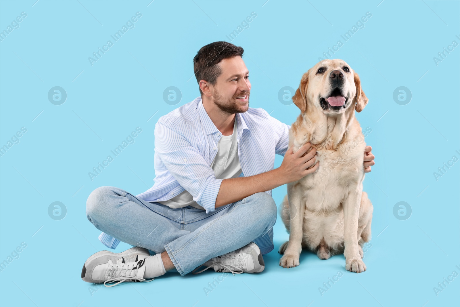Photo of Man hugging with adorable Labrador Retriever dog on light blue background. Lovely pet