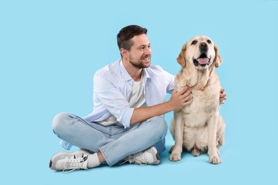 Man hugging with adorable Labrador Retriever dog on light blue background. Lovely pet