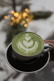 Woman holding cup of fresh matcha latte outdoors in winter, closeup