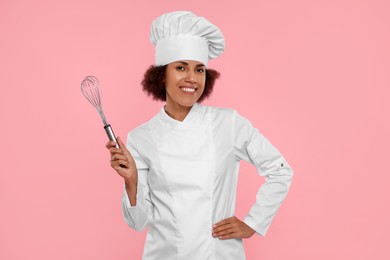 Photo of Happy female chef in uniform holding whisk on pink background