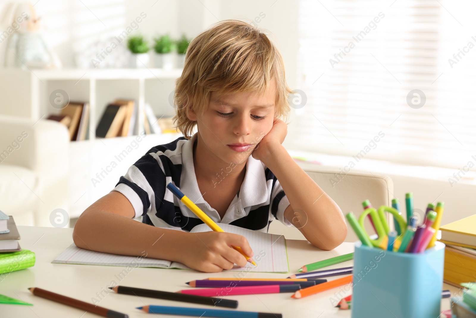 Photo of Bored little boy doing homework at table indoors