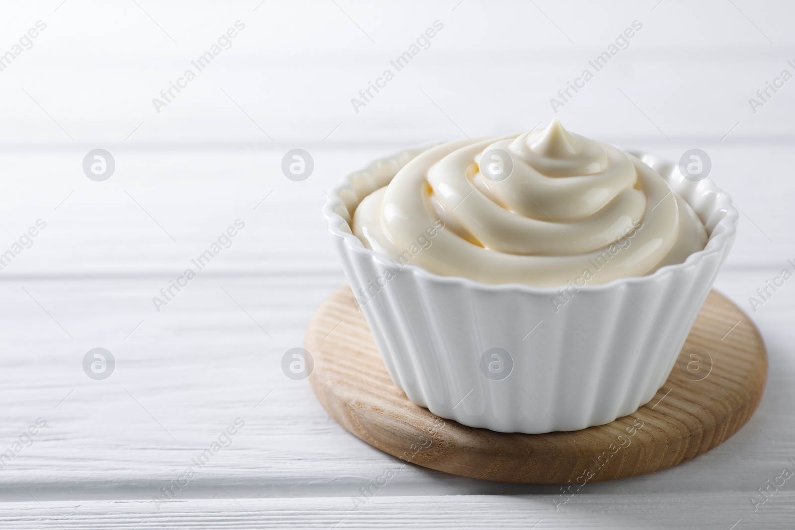 Photo of Fresh mayonnaise sauce in bowl on white wooden table, closeup. Space for text