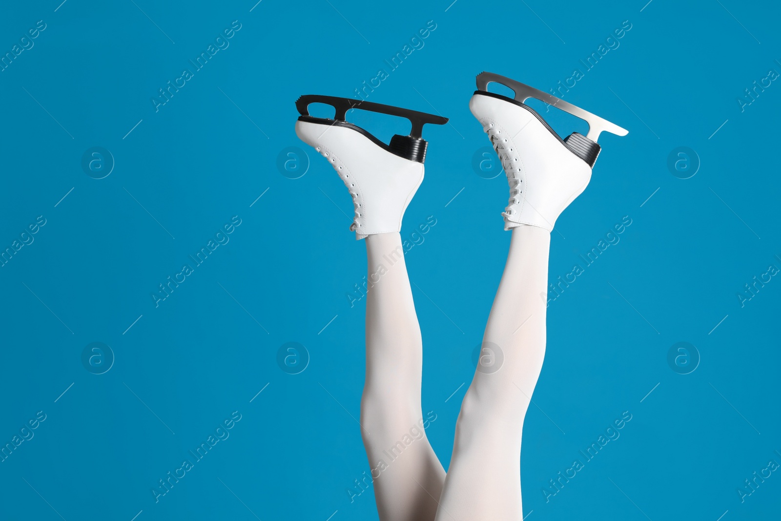 Photo of Woman in elegant white ice skates on light blue background, closeup of legs. Space for text