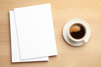 Photo of Blank paper sheets for brochure and cup of coffee on wooden background, flat lay. Mock up