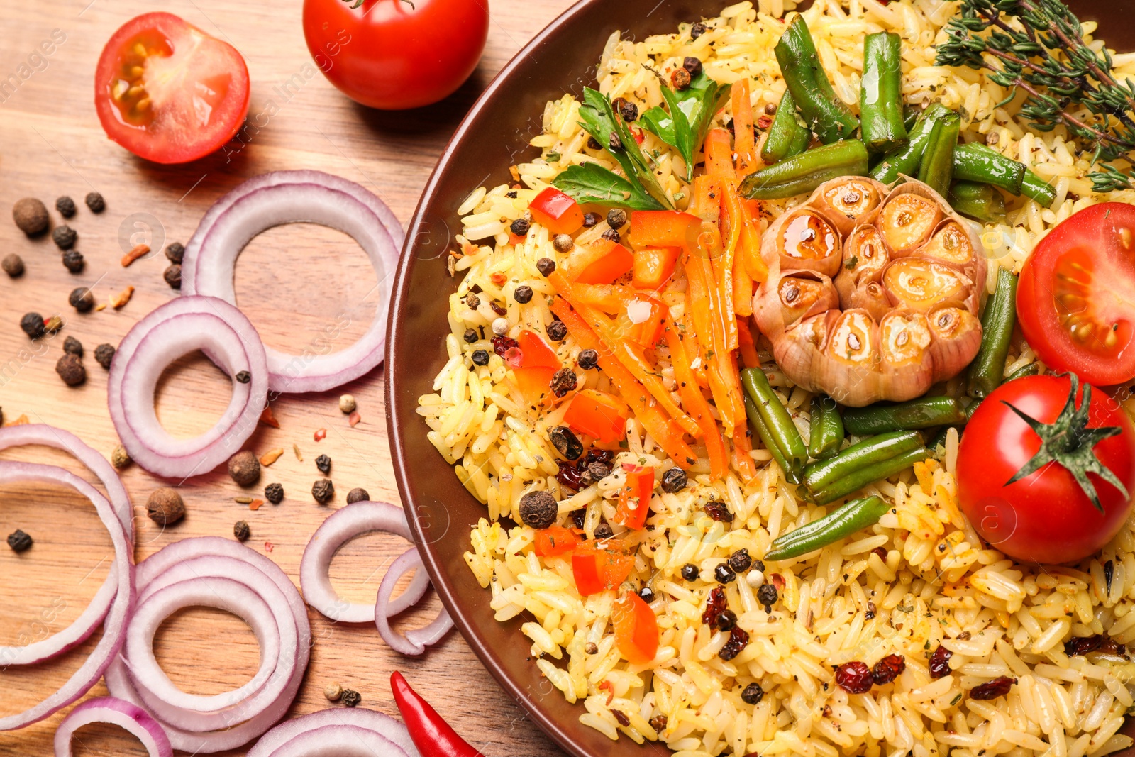 Photo of Tasty rice pilaf with vegetables on wooden table, flat lay