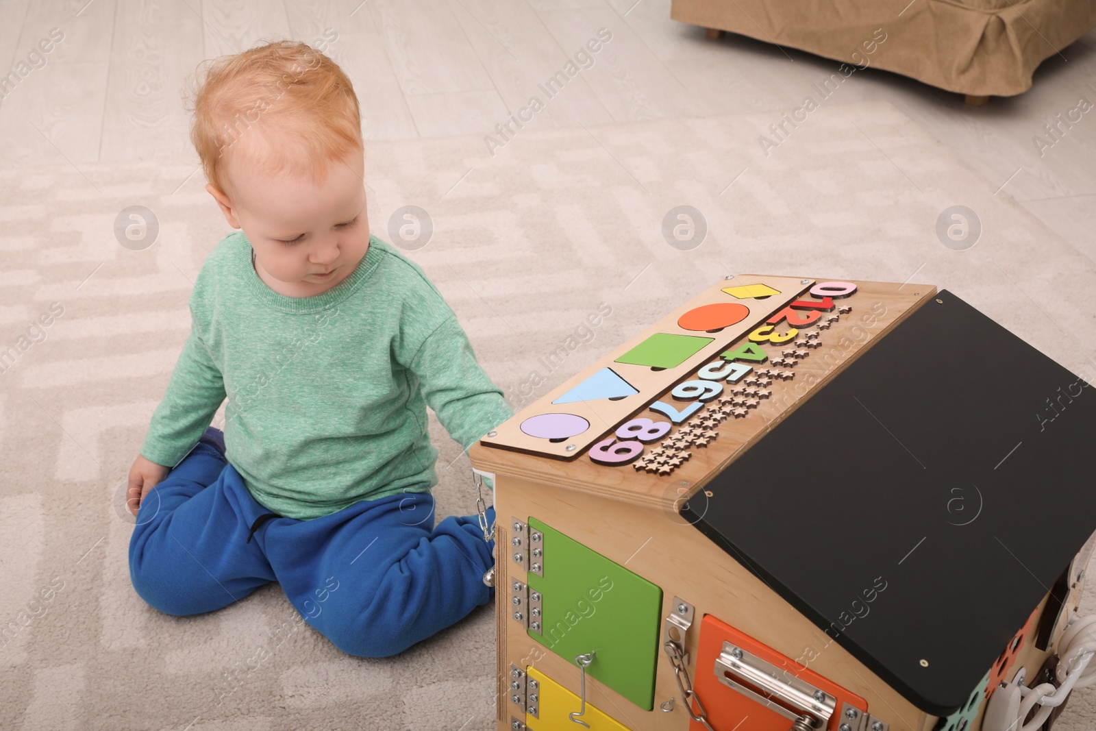 Photo of Cute little boy playing with busy board house on floor at home