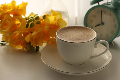 Morning coffee, alarm clock and flowers on white table indoors, space for text