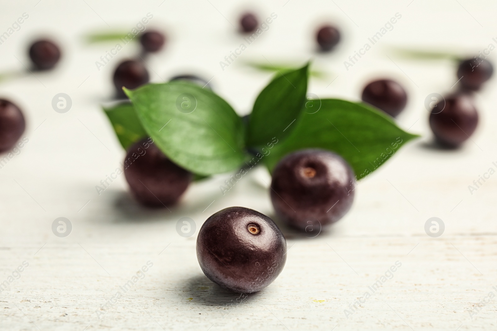 Photo of Fresh acai berries and leaves on wooden table, closeup