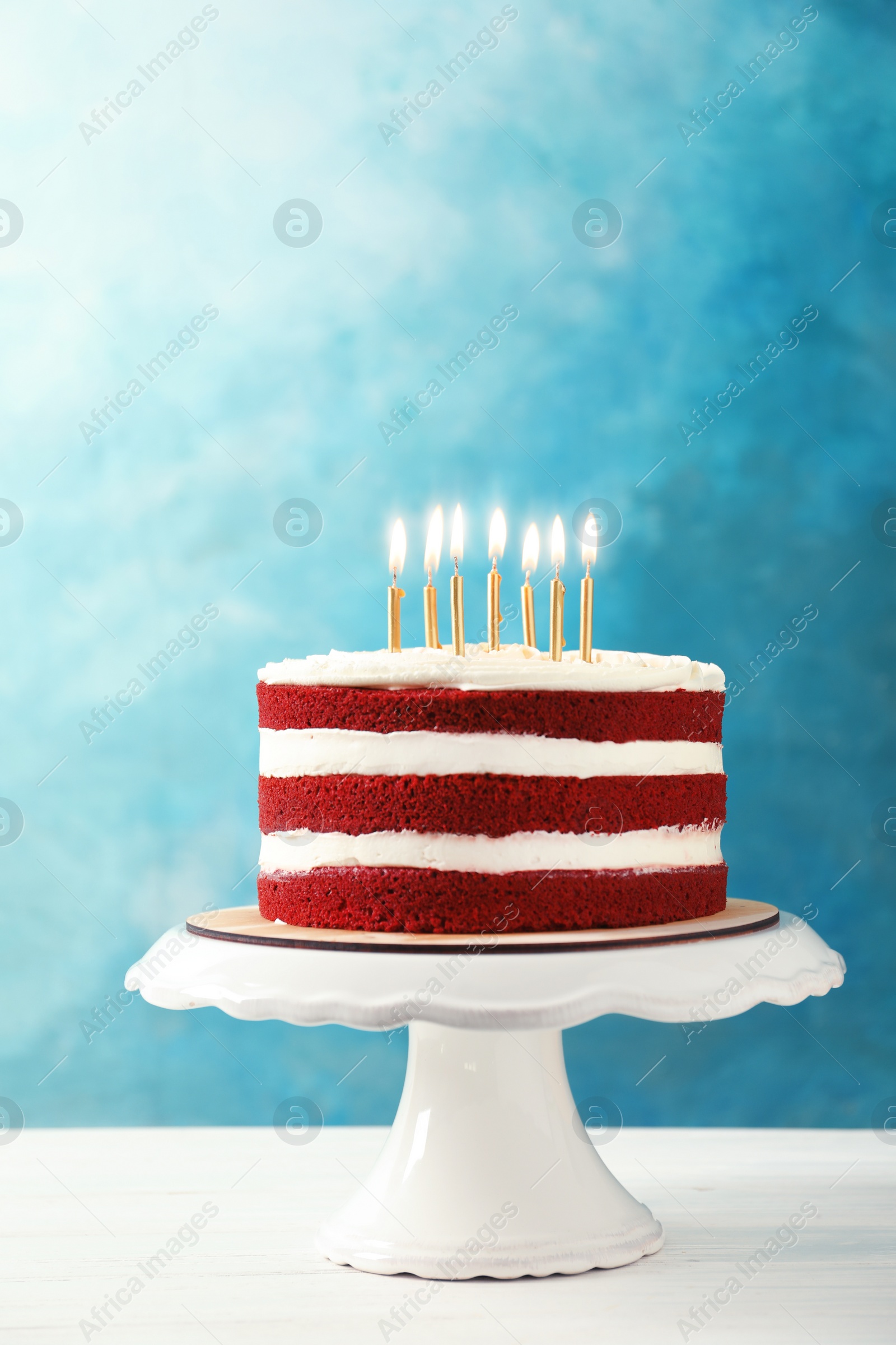 Photo of Delicious homemade red velvet cake with candles on table against color background