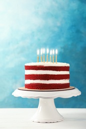 Delicious homemade red velvet cake with candles on table against color background