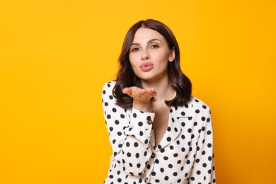 Beautiful young woman blowing kiss on yellow background