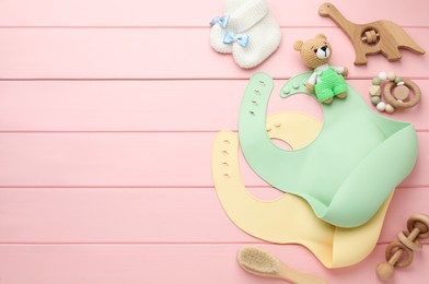 Photo of Flat lay composition with silicone baby bibs, toys and accessories on pink wooden background. Space for text