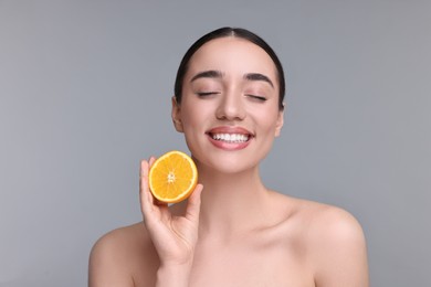 Beautiful young woman with piece of orange on grey background