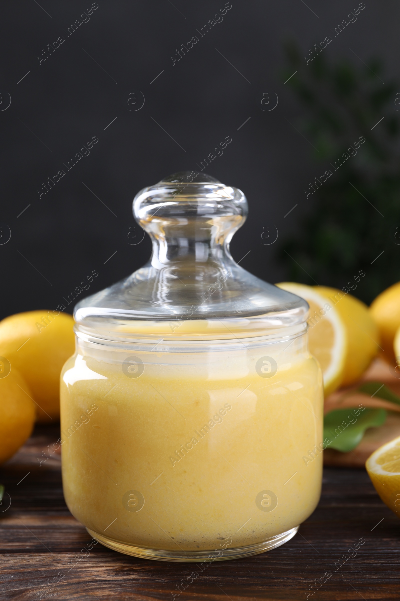 Photo of Delicious lemon curd in glass jar and fresh citrus fruits on wooden table
