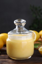 Delicious lemon curd in glass jar and fresh citrus fruits on wooden table