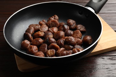 Photo of Roasted edible sweet chestnuts in frying pan on wooden table, closeup