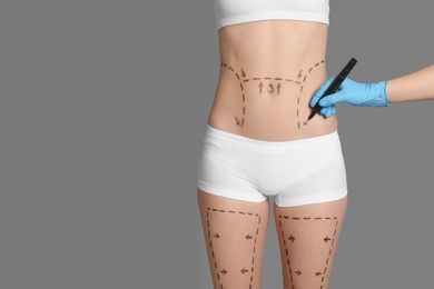 Photo of Doctor drawing marks on female belly for cosmetic surgery operation against color background