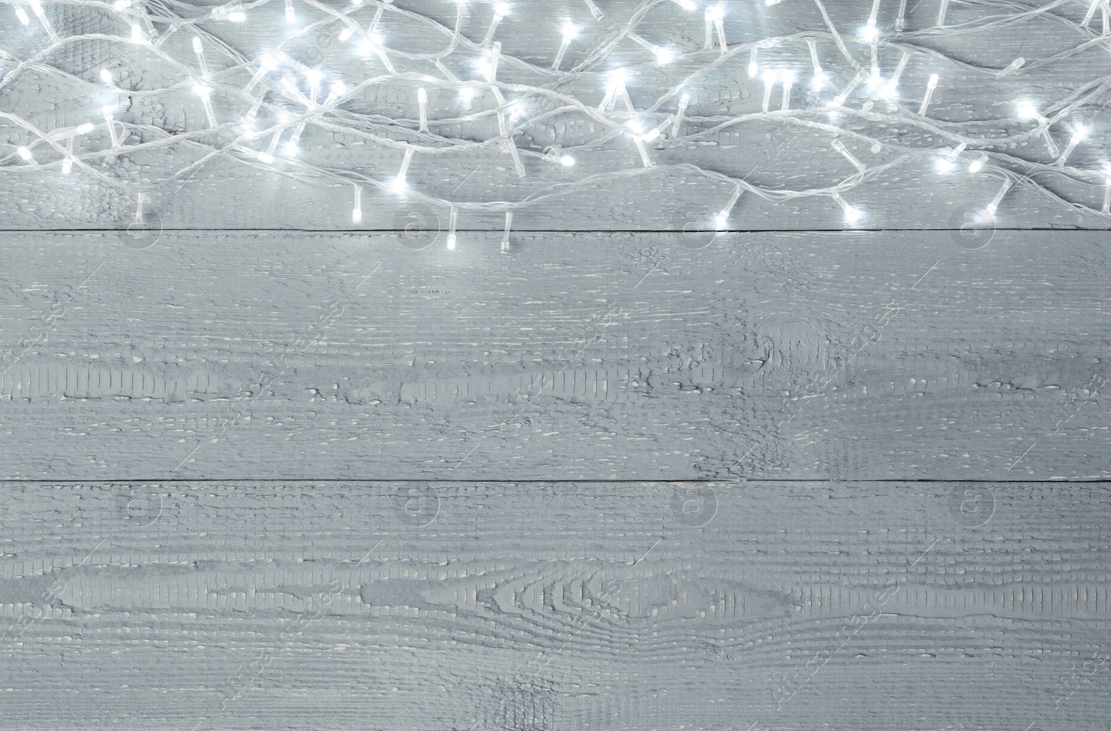 Photo of Glowing Christmas lights on wooden background, top view. Space for text