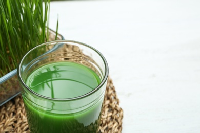 Photo of Glass of wheat grass juice on table, closeup. Space for text