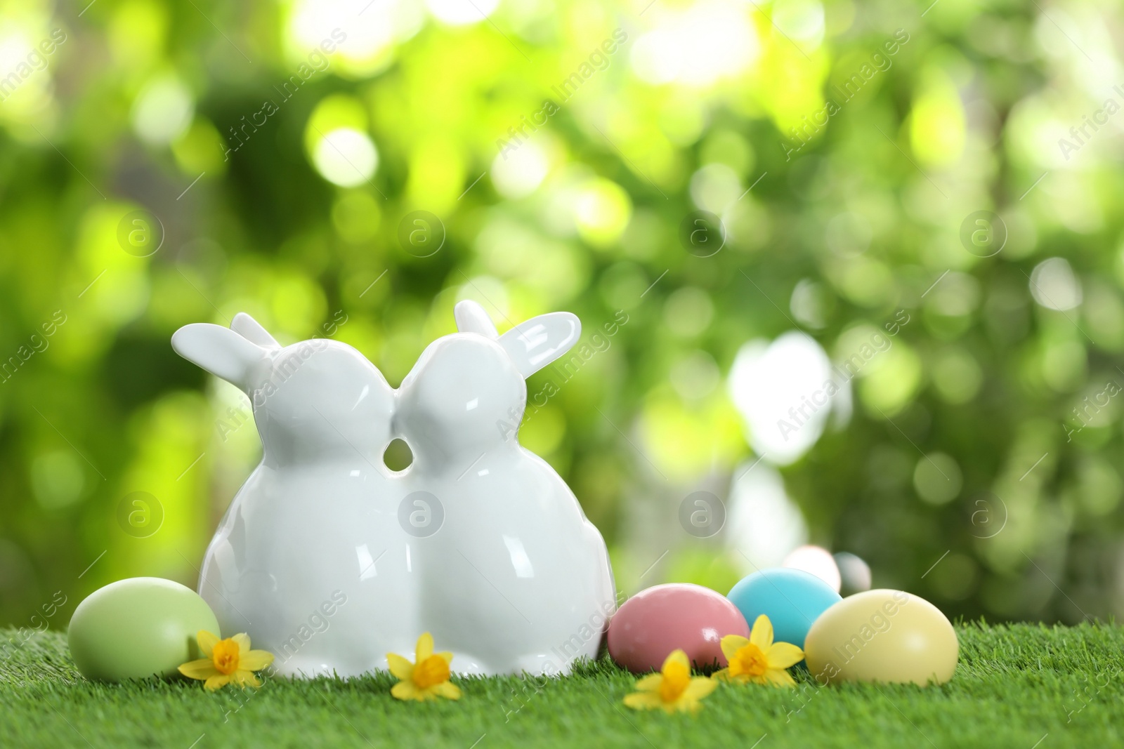 Photo of Cute ceramic Easter bunnies and dyed eggs on green grass against blurred background, space for text