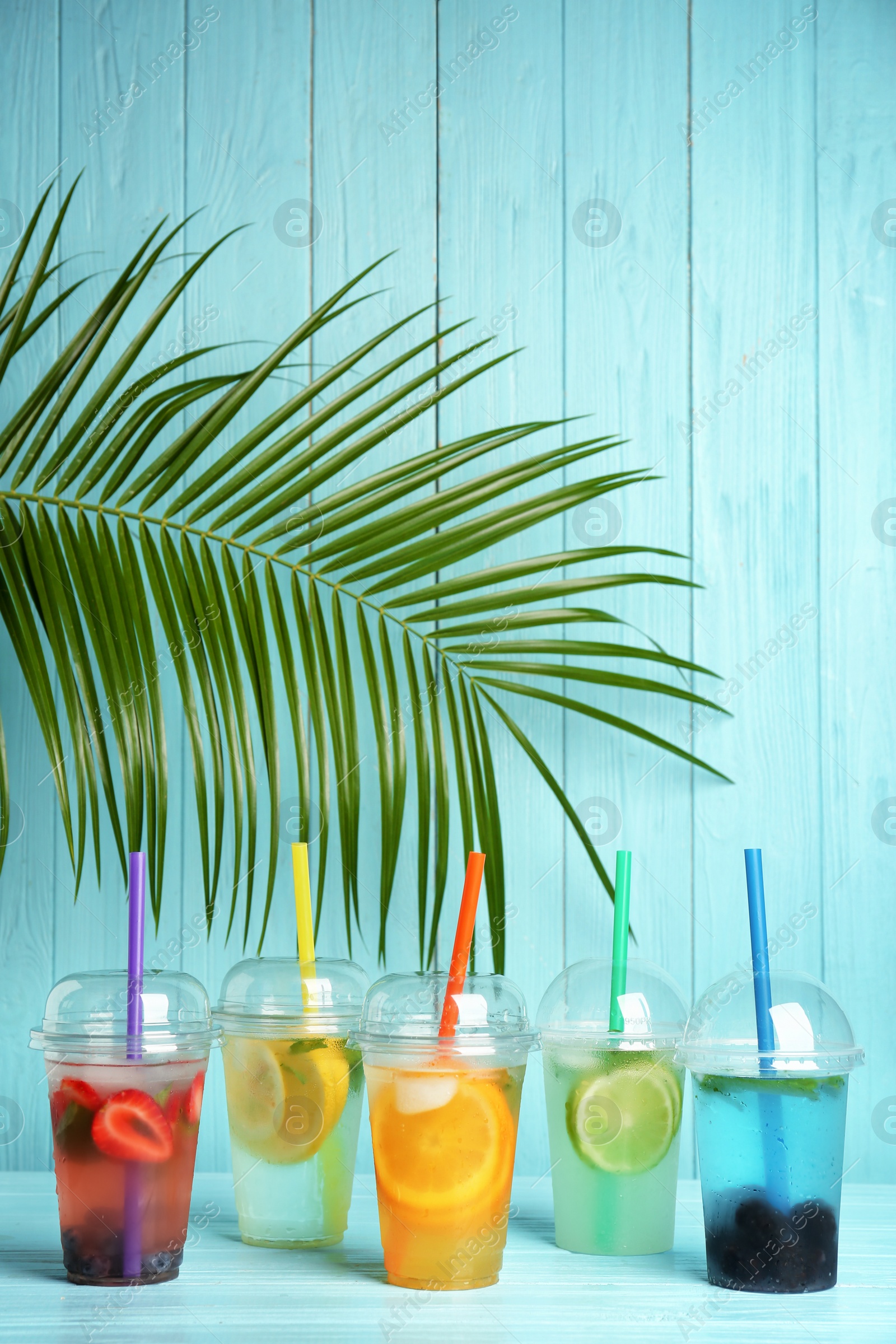 Photo of Plastic cups with lemonades on table against color background