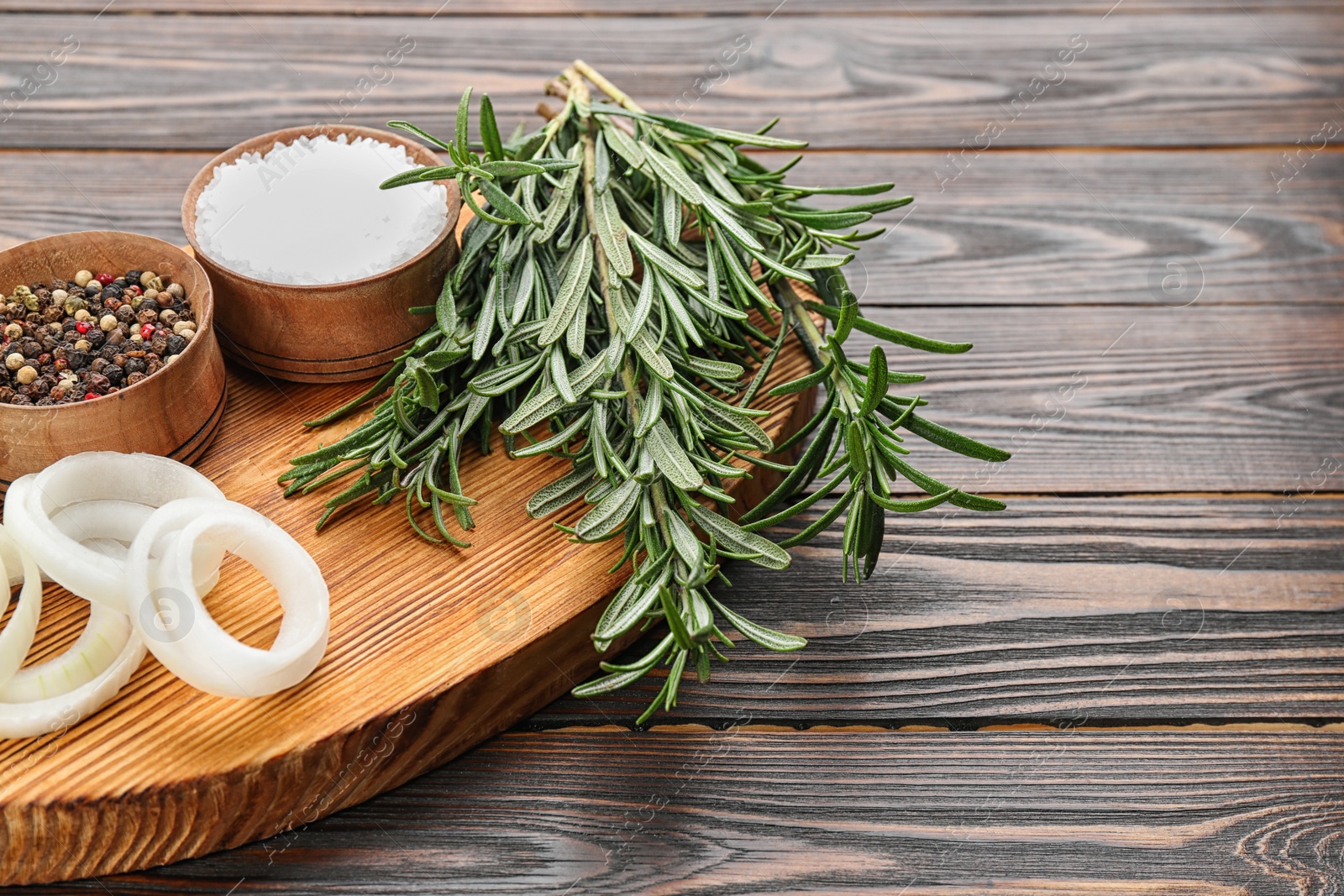 Photo of Fresh rosemary, onion and spices on wooden table, closeup