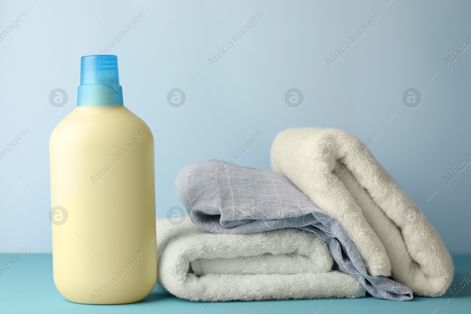 Photo of Bottle of fabric softener and towels on light blue table