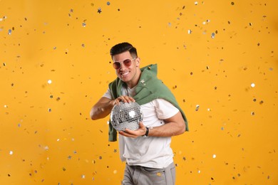 Photo of Happy man with disco ball and confetti on yellow background