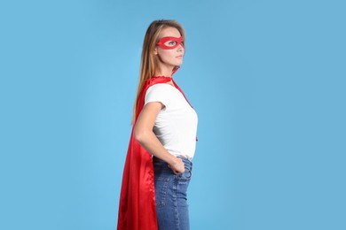 Confident woman wearing superhero cape and mask on light blue background