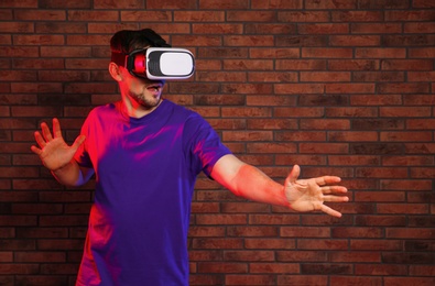 Emotional man playing video games with virtual reality headset near brick wall. Space for text