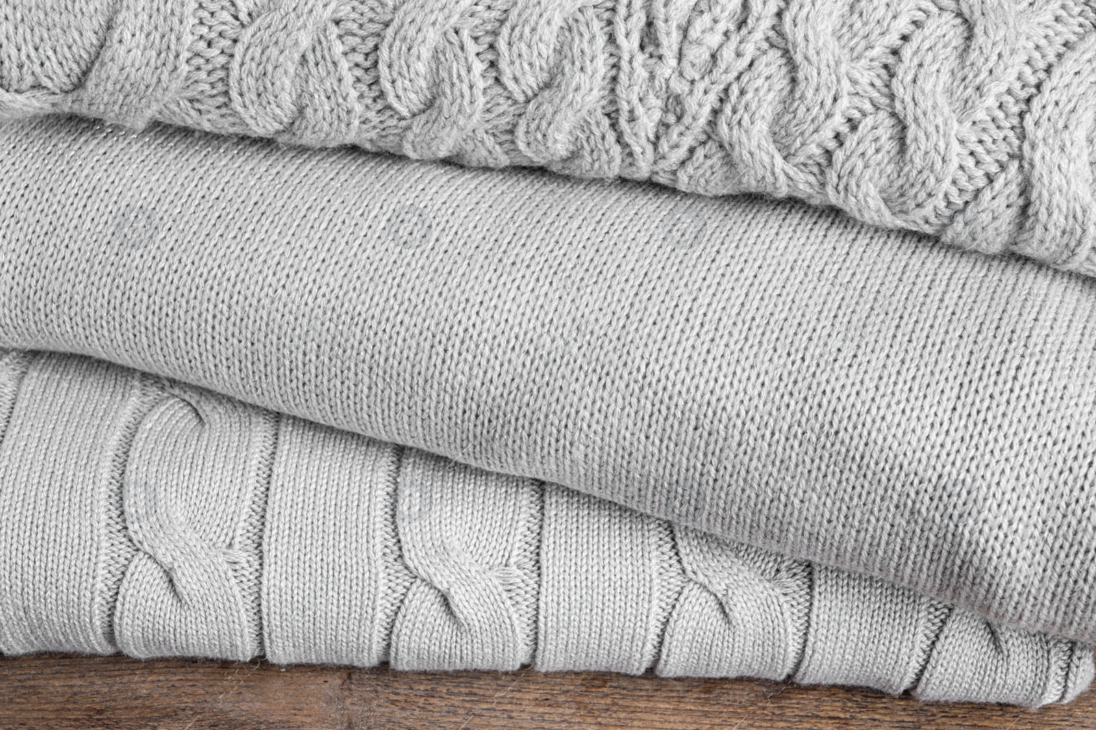 Image of Stack of folded warm sweaters on wooden table, closeup