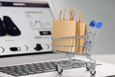Photo of Mini cart with shopping bags on laptop against light grey background, closeup. Online store