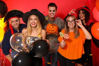 Happy friends in costumes with Halloween party accessories on red background
