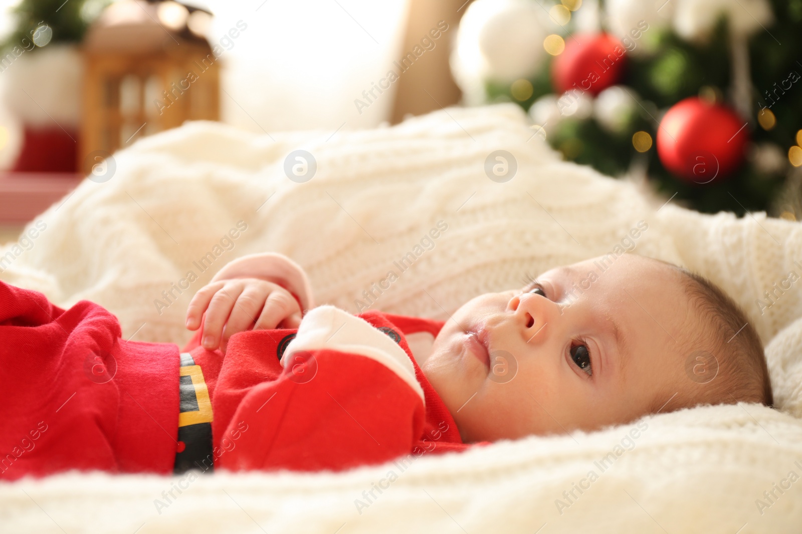 Photo of Cute little baby on knitted blanket in room decorated for Christmas