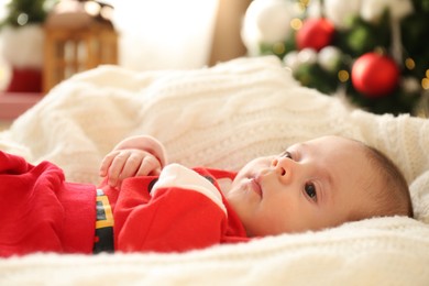 Cute little baby on knitted blanket in room decorated for Christmas