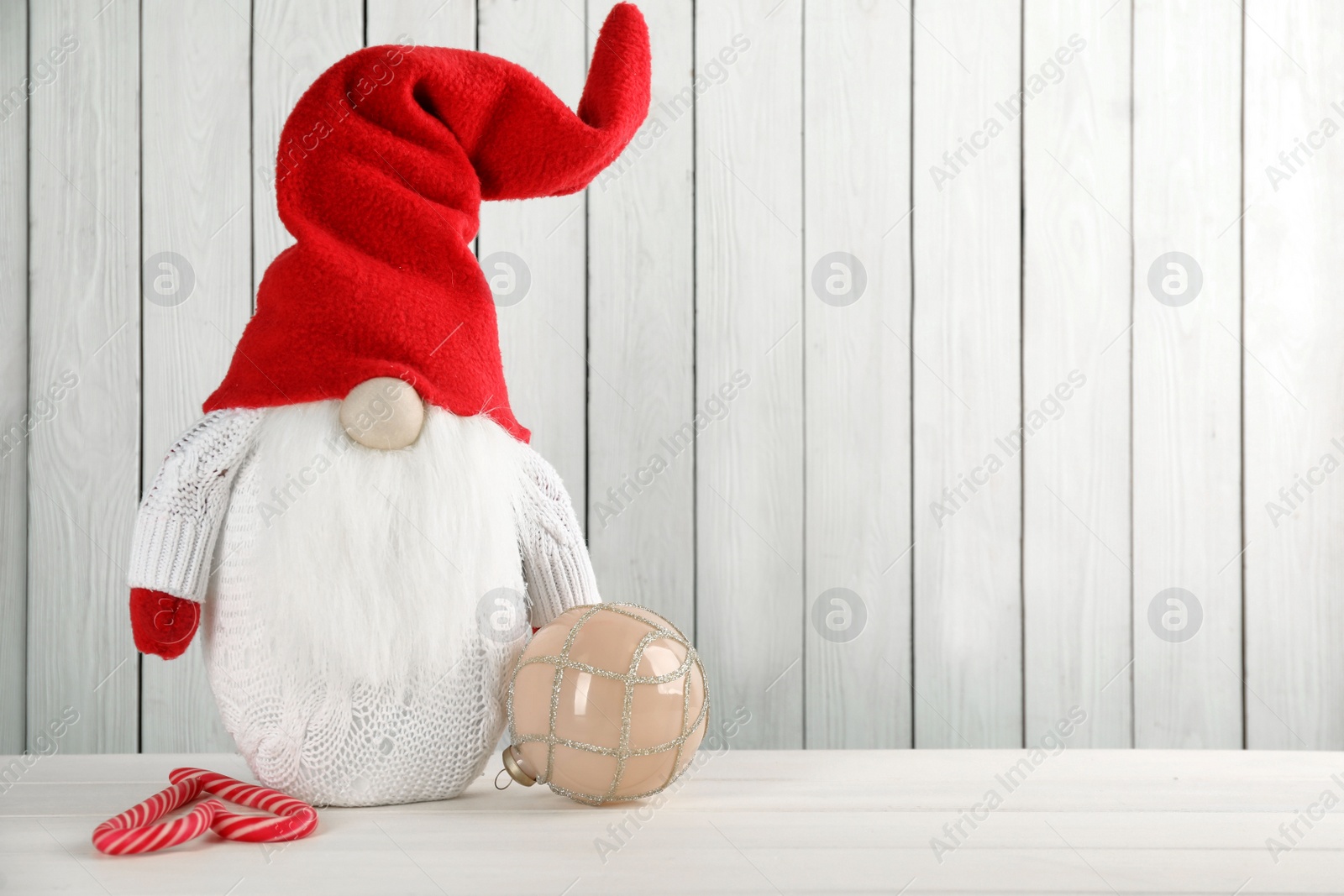 Photo of Cute Christmas gnome, festive ball and candy canes on table against white wooden background. Space for text