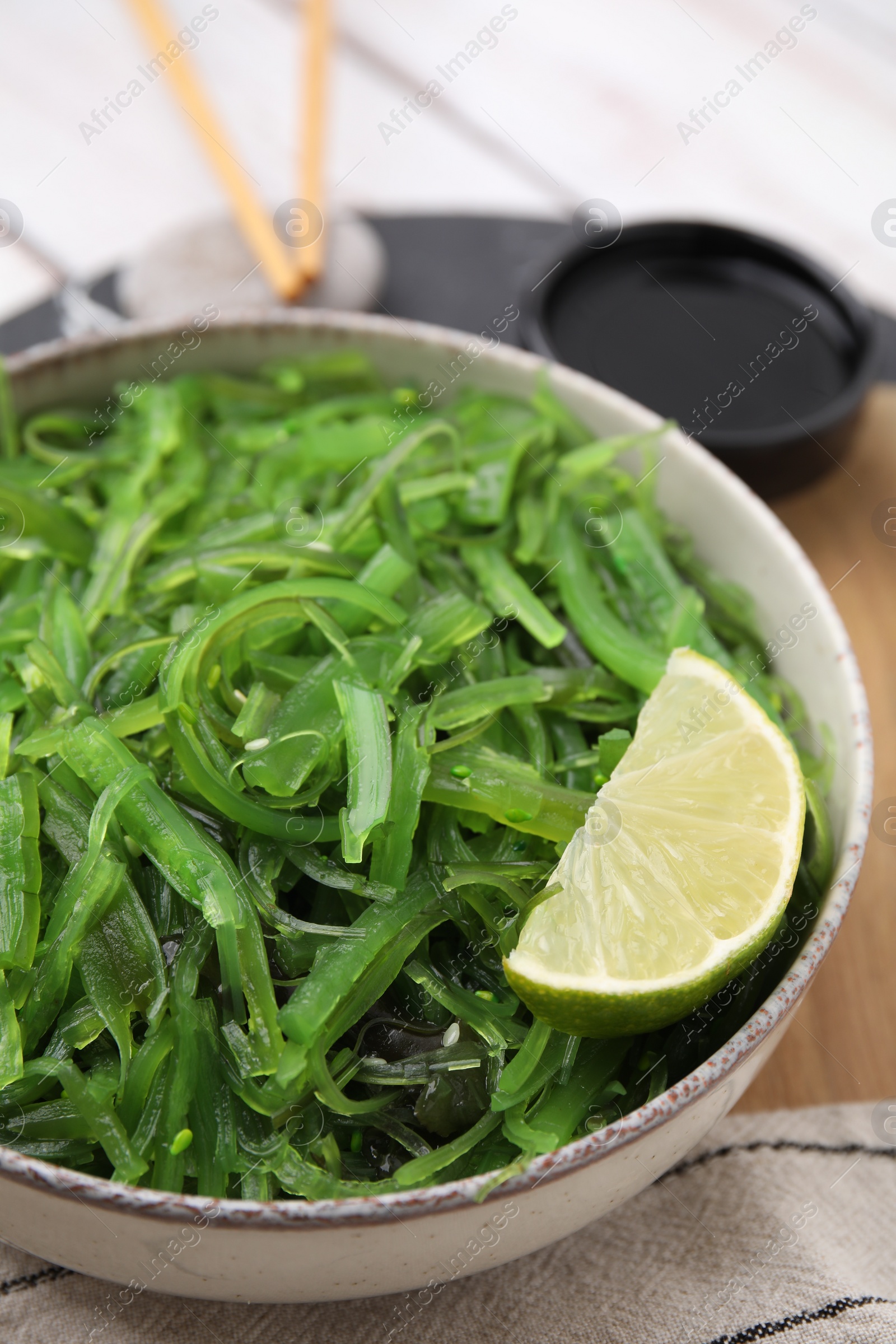 Photo of Tasty seaweed salad in bowl served on wooden table, closeup