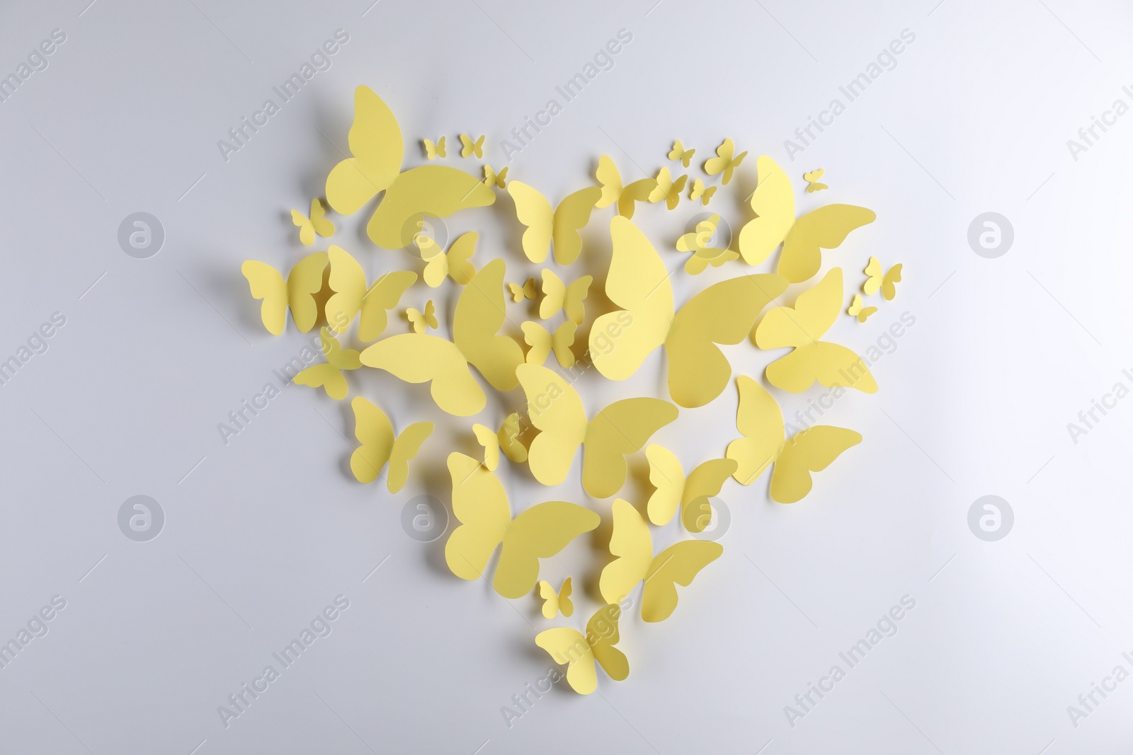 Photo of Heart shape made of yellow paper butterflies on white background, top view