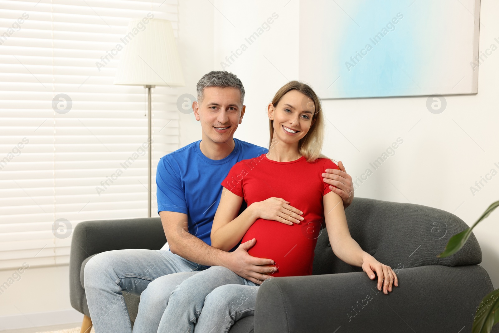 Photo of Young family housing concept. Pregnant woman with her husband on sofa at home