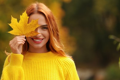 Photo of Smiling woman covering eye with autumn leaf outdoors. Space for text