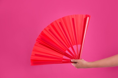 Woman holding red hand fan on pink background, closeup