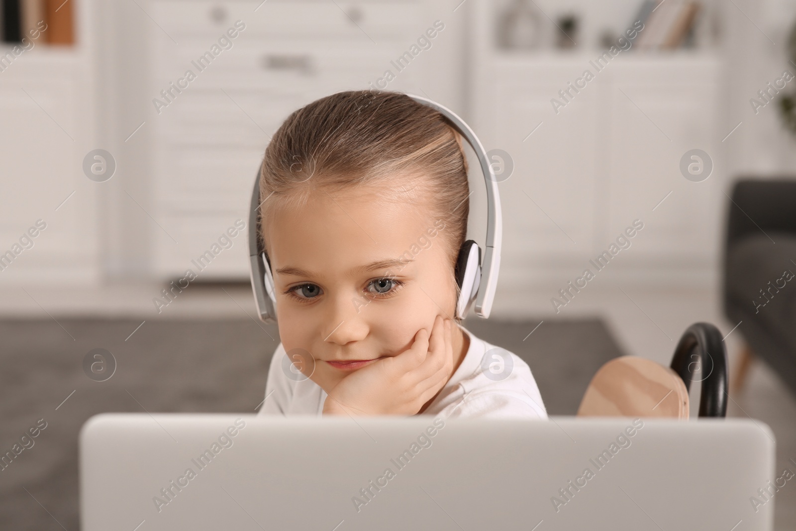 Photo of Little girl in headphones using laptop at home. Internet addiction