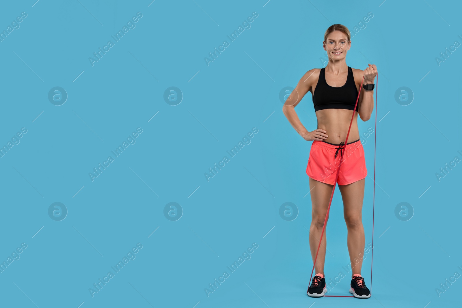 Photo of Woman exercising with elastic resistance band on light blue background. Space for text