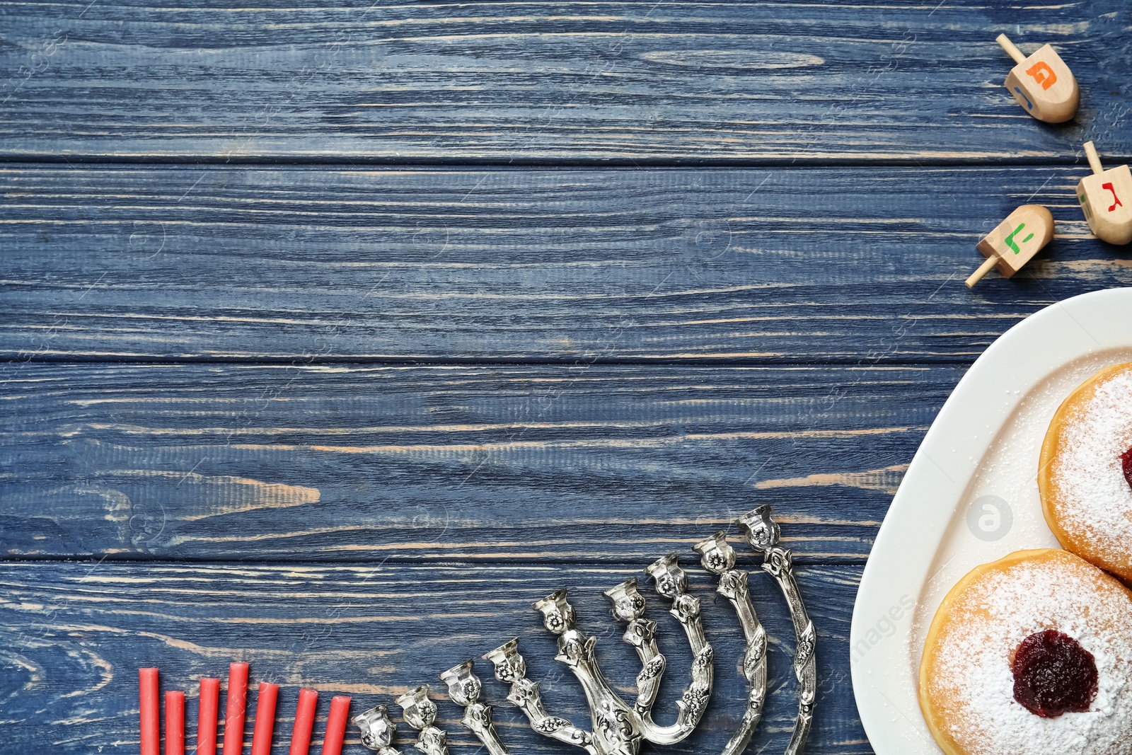 Photo of Flat lay composition of menorah, red candles, dreidels with He, Pe, Nun, Gimel letters and sufganiyot on blue wooden table, space for text. Hanukkah symbols