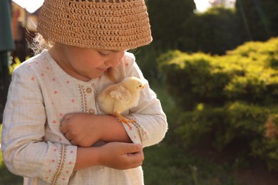 Photo of Cute little girl with chick outdoors, space for text. Baby animal