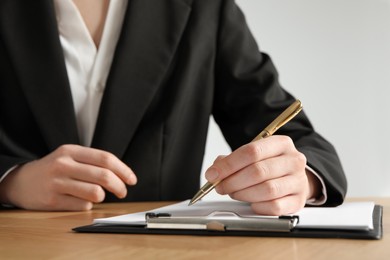 Photo of Woman with pen and clipboard at wooden table, closeup